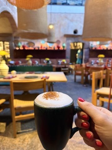 A cappuccino held up in a colorful San Miguel café