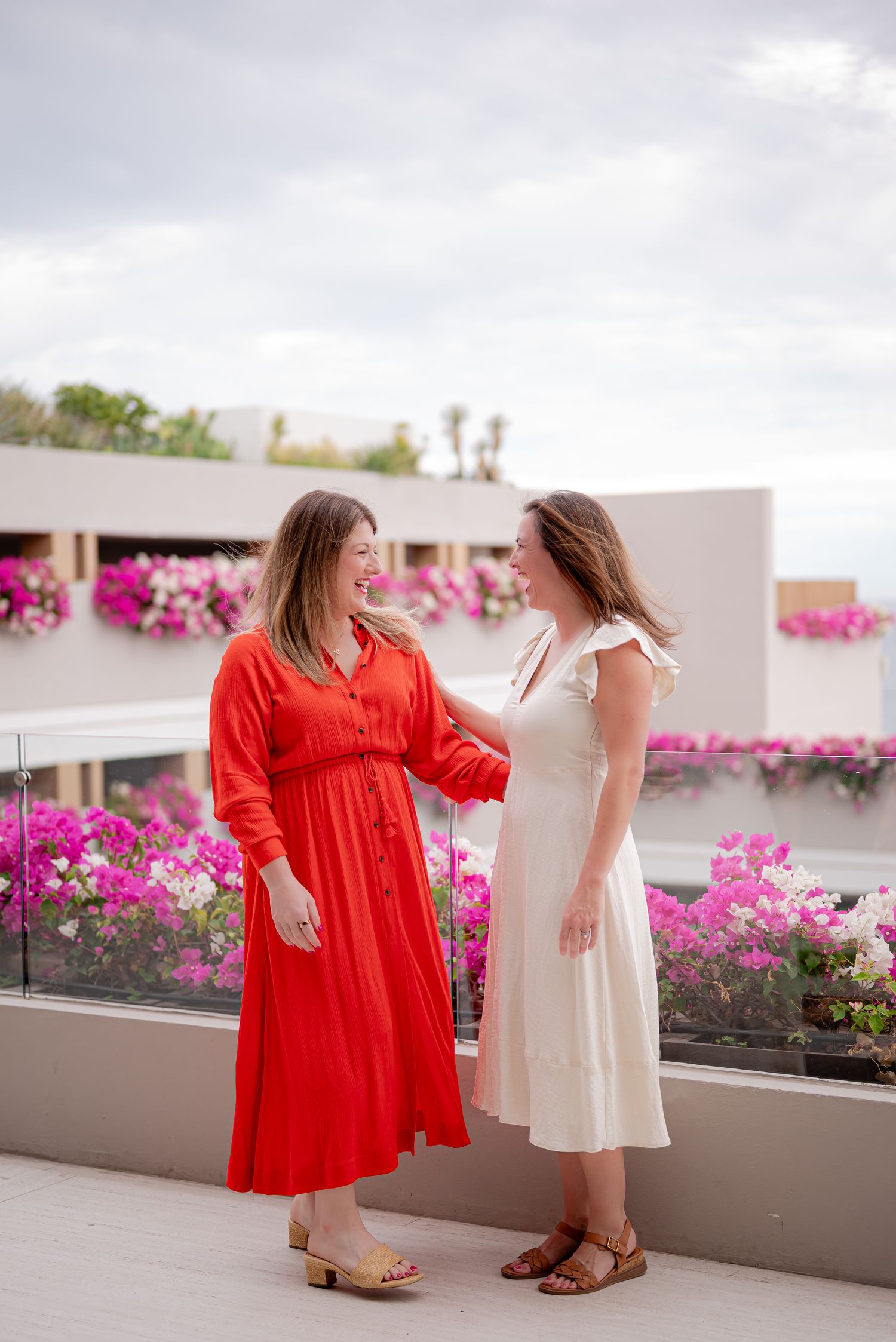Katie and Tracy laughing together on a flower-lined terrace
