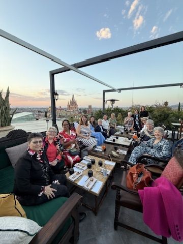 A group of women gathered on a rooftop at sunset with the Parroquia in the distance