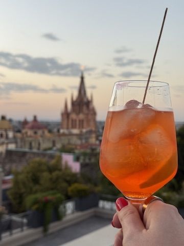 An Aperol spritz raised at golden hour with the Parroquia in the background