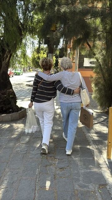 Two women walking arm in arm down a tree-lined street